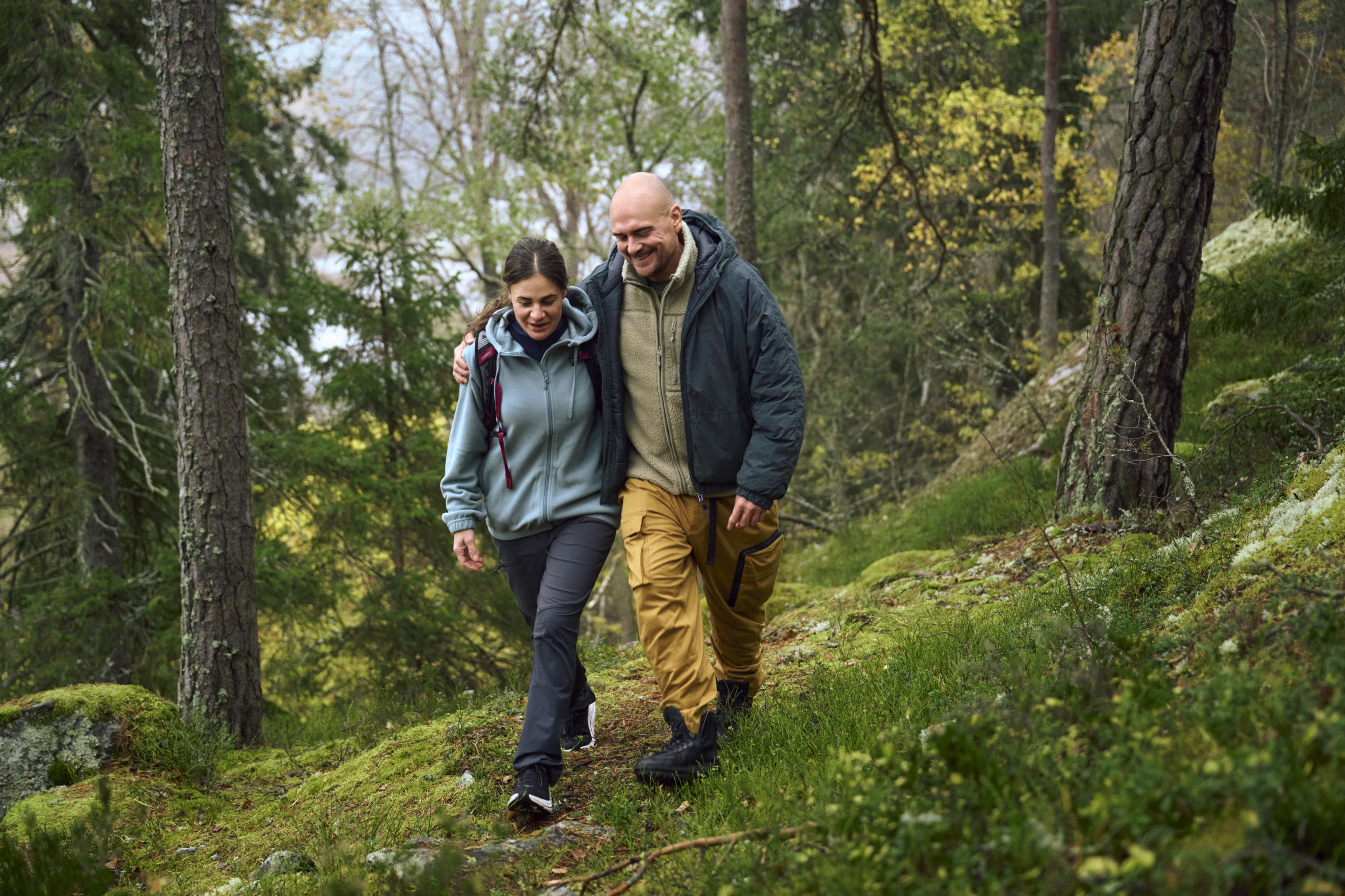 A man and a woman walking together on a forest trail. The man has his arm around the woman. 