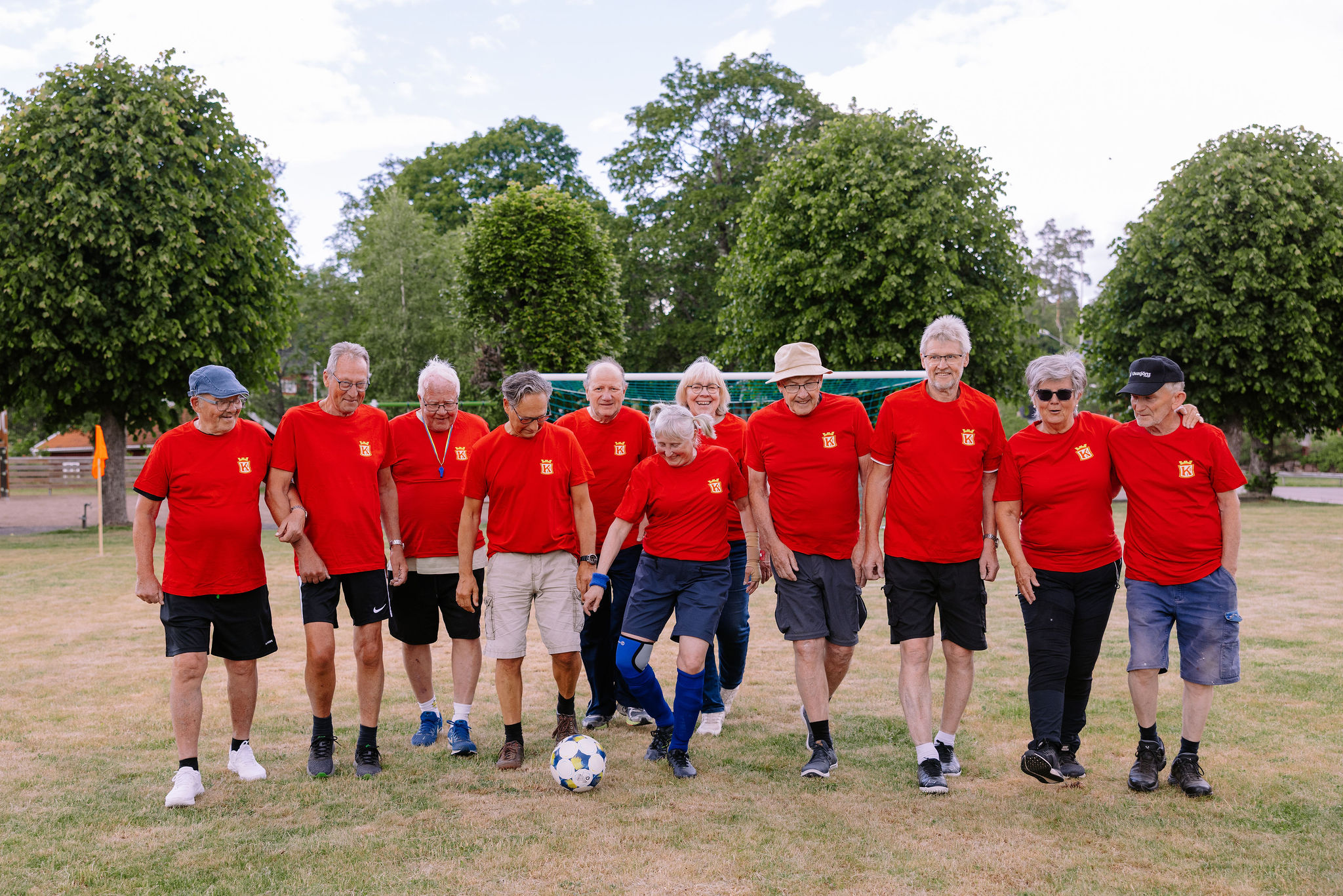 Elva pigga och glada pensionärer på fotbollsplanen i Fröseke iklädda Kronofrs IF:s röda fotbollströjor. 